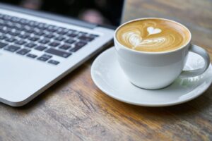 A cup of coffee near a laptop on a desk.